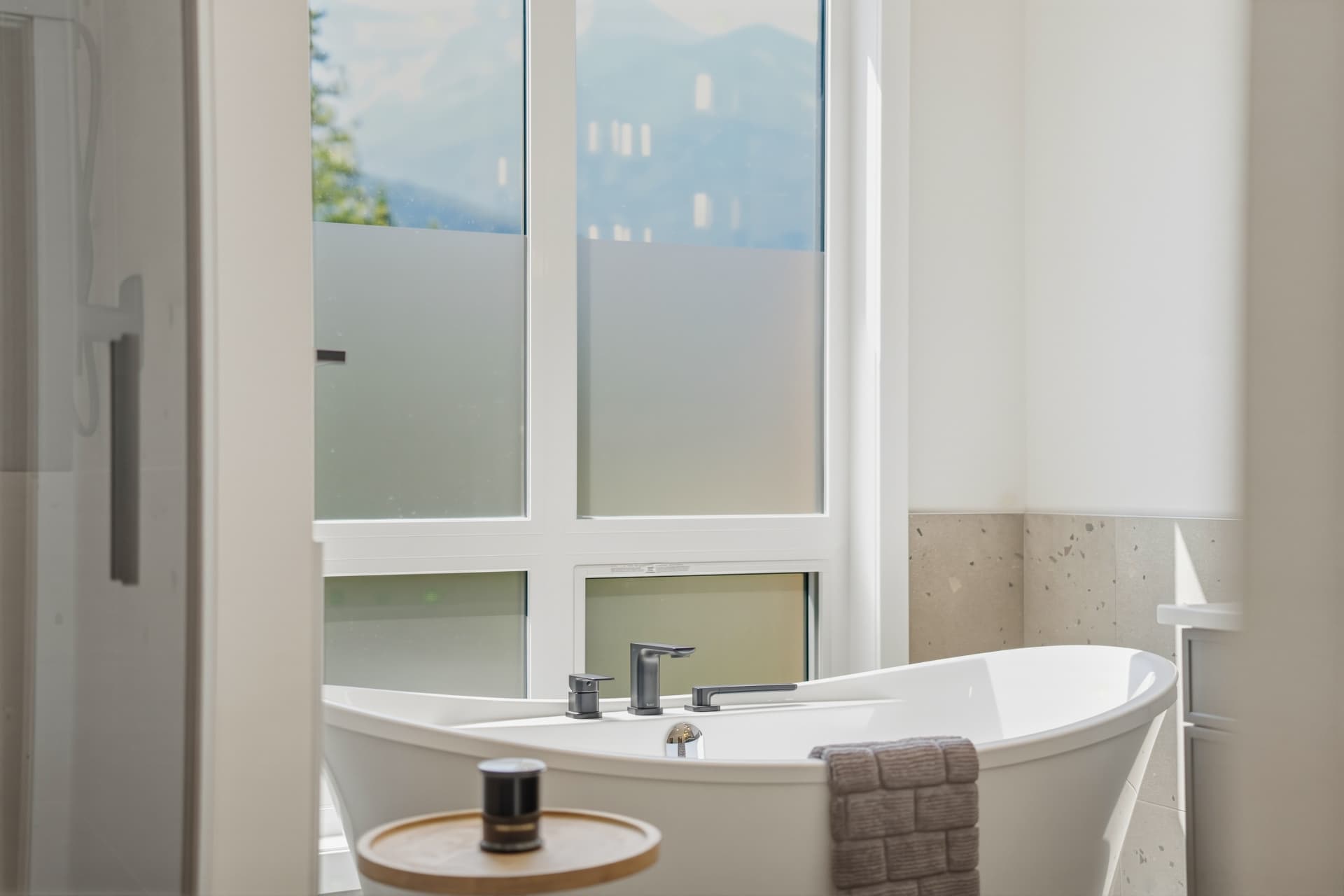 Freestanding soaker tub beside frosted mountain-view windows